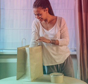 A woman excitedly reaching into a brown paper bag for takeaway food