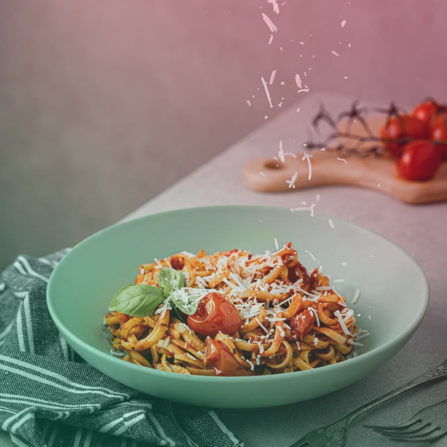 parmesan cheese being sprinked onto a green bowl of pasta with fresh tomato sauce